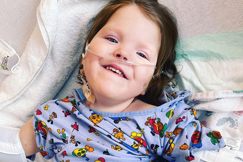 Photo of girl lying on blankets wearing hospital gown featuring cartoon characters.