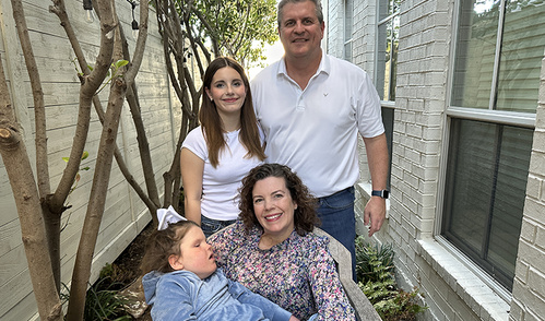 Four members of a family pose together for a portrait outdoors between two buildings.